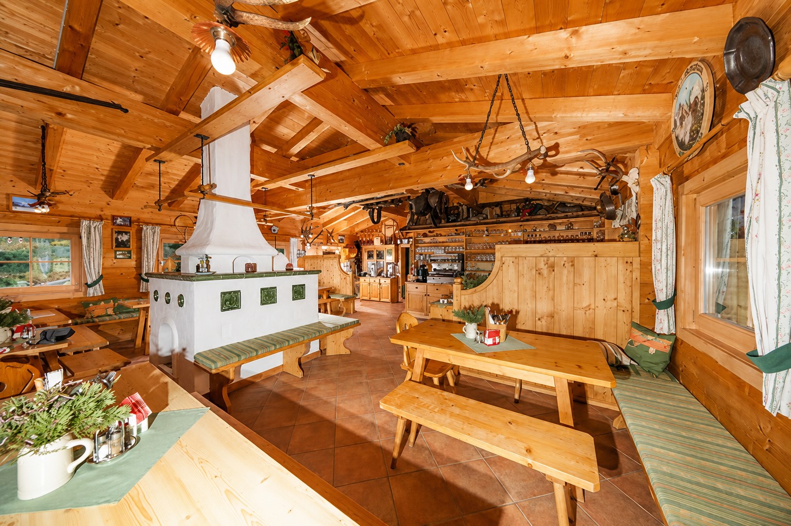 Die großzügige Holzstube der Hütte GUD-SBG mit Kachelofen und langen Tischen